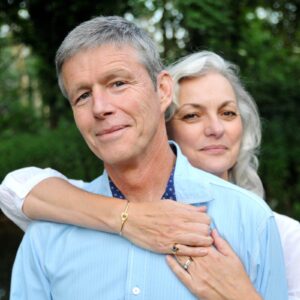 man with woman standing behind him and arms around him.