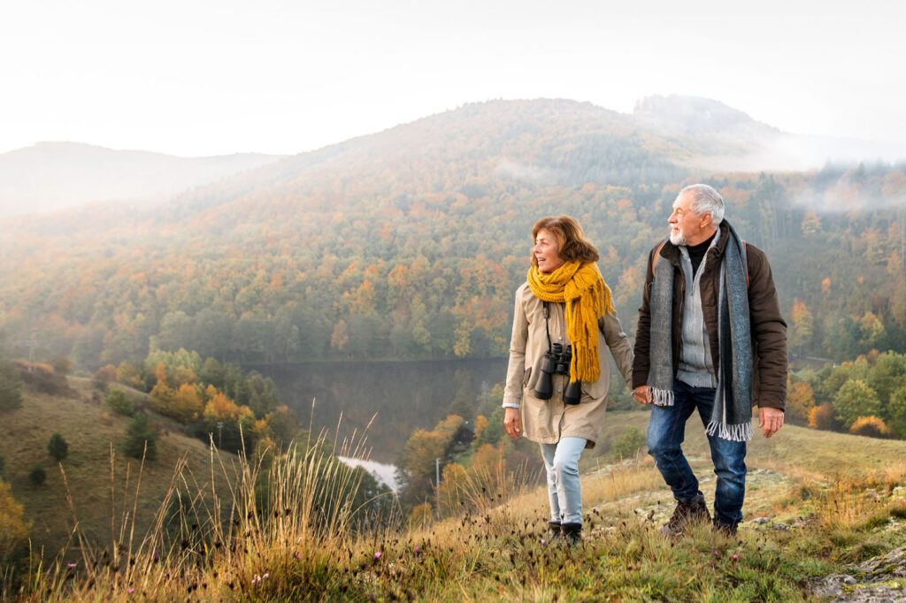 older man and woman walking during the fall in the mountains.
